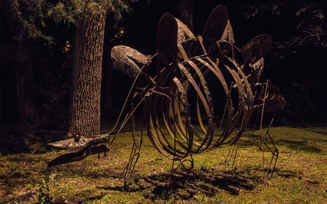 outdoor metal sculpture of dinosaur illuminated at night